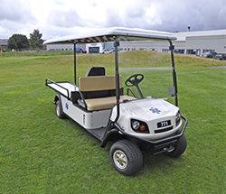 White EMT golf cart with a white roof on a lawn in front of a building.